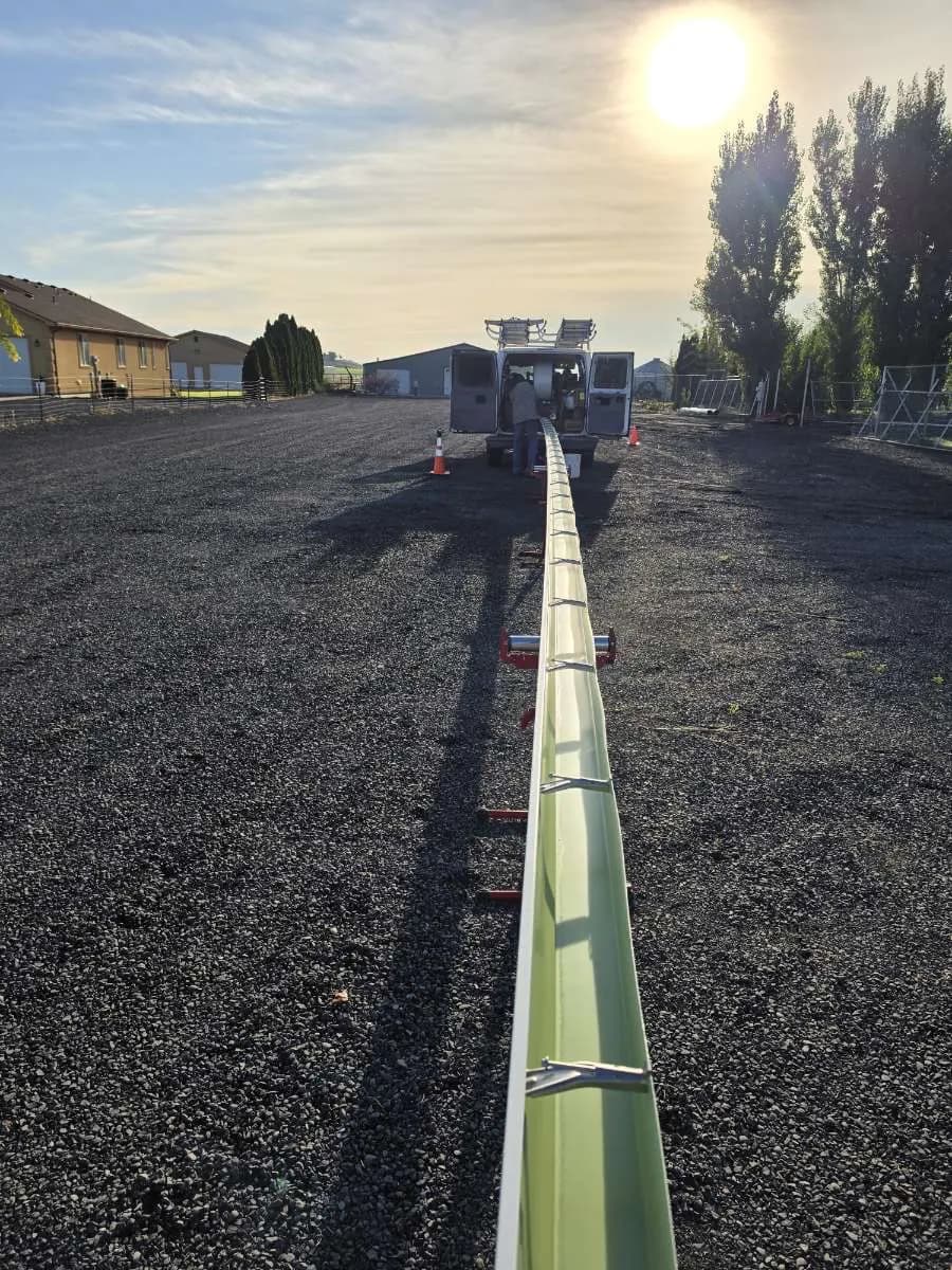 One continuous on-site seamless gutter run stretching across a gravel lot at sunrise